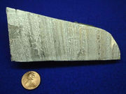 A piece of aluminium metal about 15 centimetres long, with a U.S. cent included for scale.