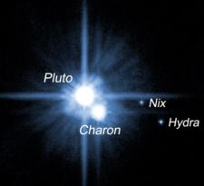 Pluto and its three known moons. Pluto and Charon are the bright objects in the center, the two smaller moons are at the right and bottom, farther out.