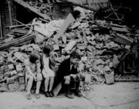 Children of an eastern suburb of London, who have been made homeless by the random bombs of the Nazi night raiders, waiting outside the wreckage of what was their home. September 1940.  (National Archives)