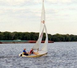 A sailboat (racing dinghy) and barge share the Mississippi River,USA.