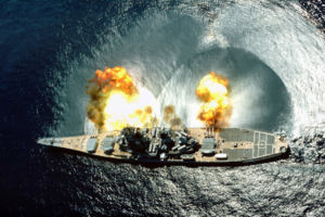 USS Iowa fires a full broadside of nine 16-inch (406 mm) / 50-caliber and six 5-inch (127 mm) / 38-calibre guns during a target exercise. Note concussion effects on the water surface, and 16-inch (406 mm) gun barrels in varying degrees of elevation.